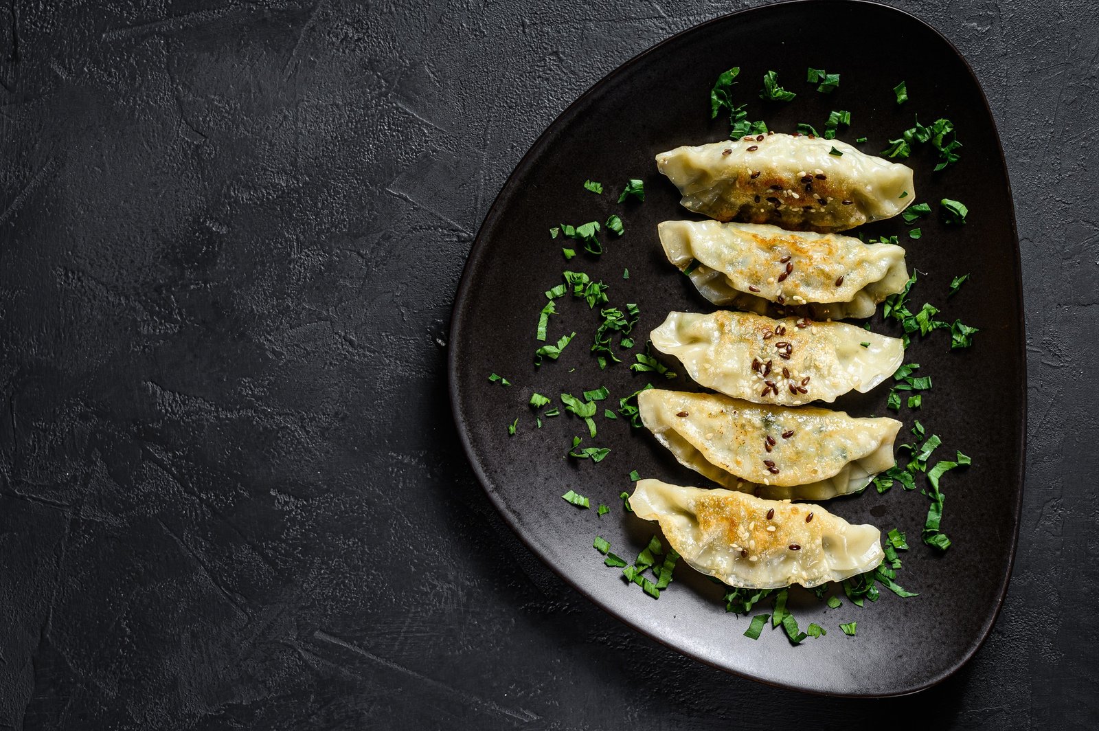 Plate of fried Japanese gyoza dumplings on rustic black table. Top view. Space for text